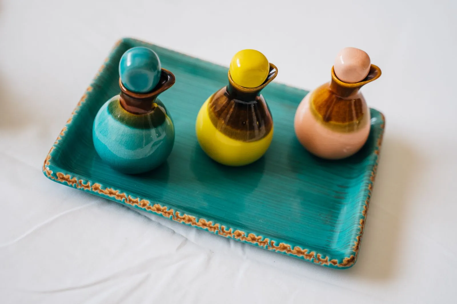 Three ceramic bottles in varying colors on a teal decorative tray.